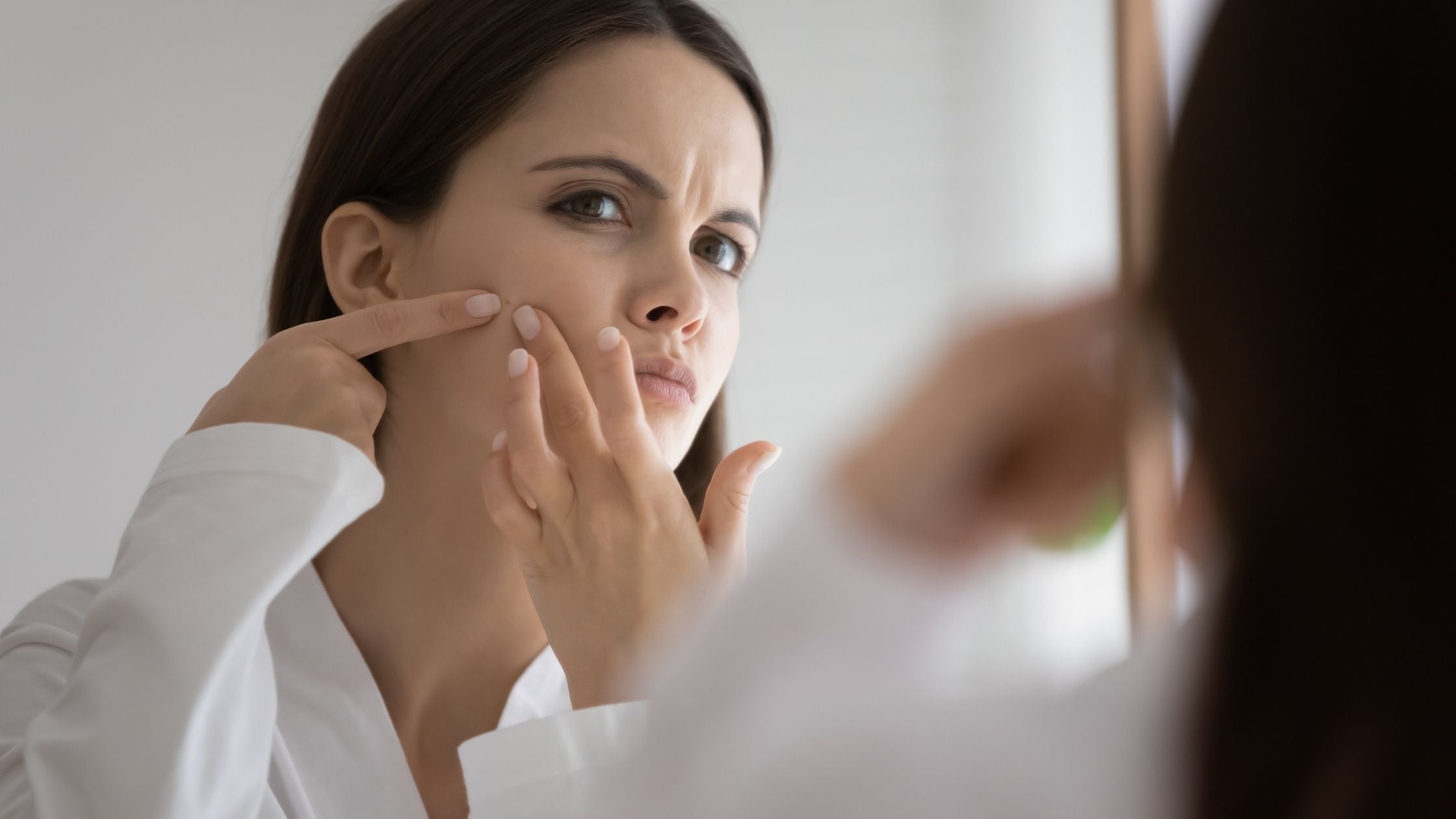 young woman looking in mirror squeezing and popping pimple